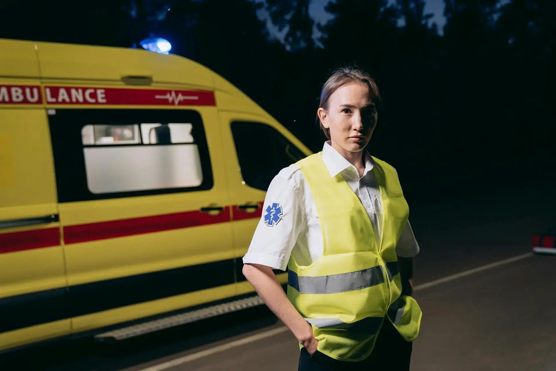 une ambulancière sur la route en gilet jaune avec son véhicule de secours derrière