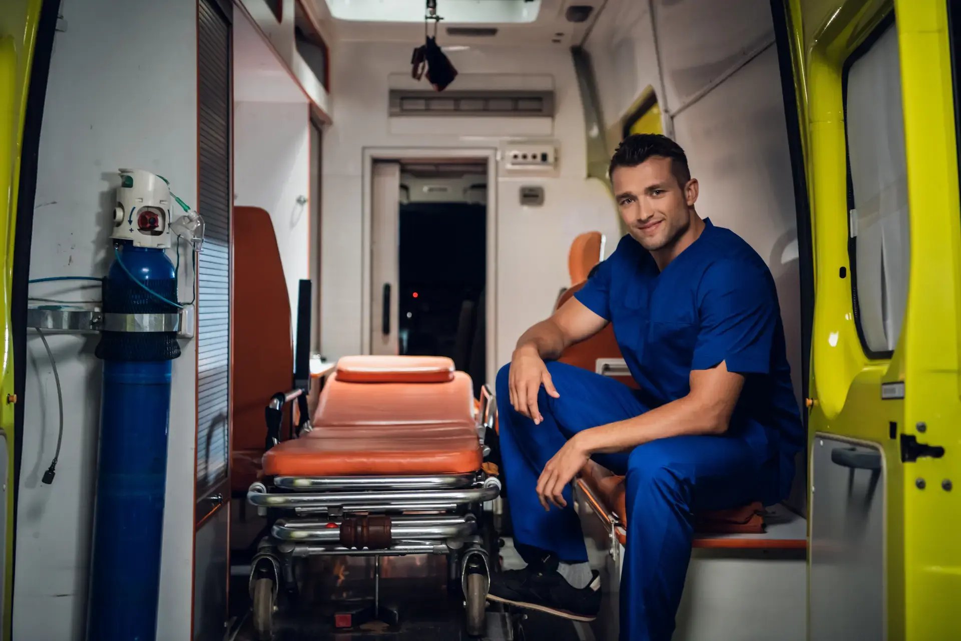 ambulancier en blouse bleu assis dans son véhicule de secours avec un brancard