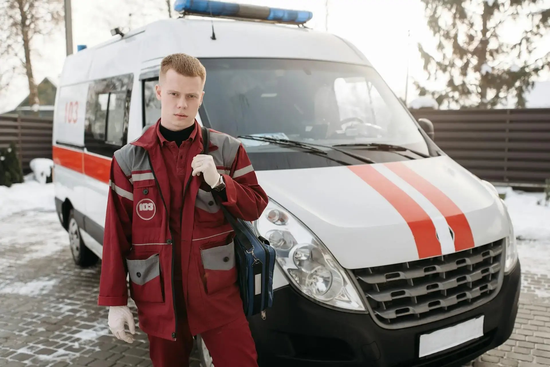 jeune ambulancier en uniforme rouge devant son véhicule
