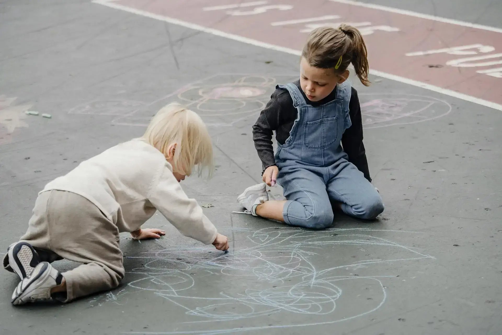 deux enfants qui dessinent à la craie sur le sol dehors