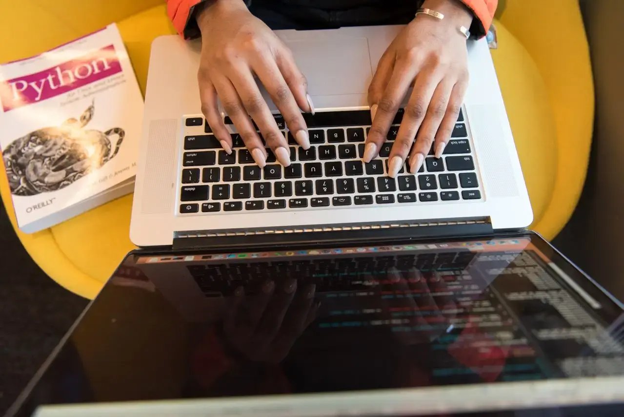 Une femme tape sur son clavier avec un livre python à côté