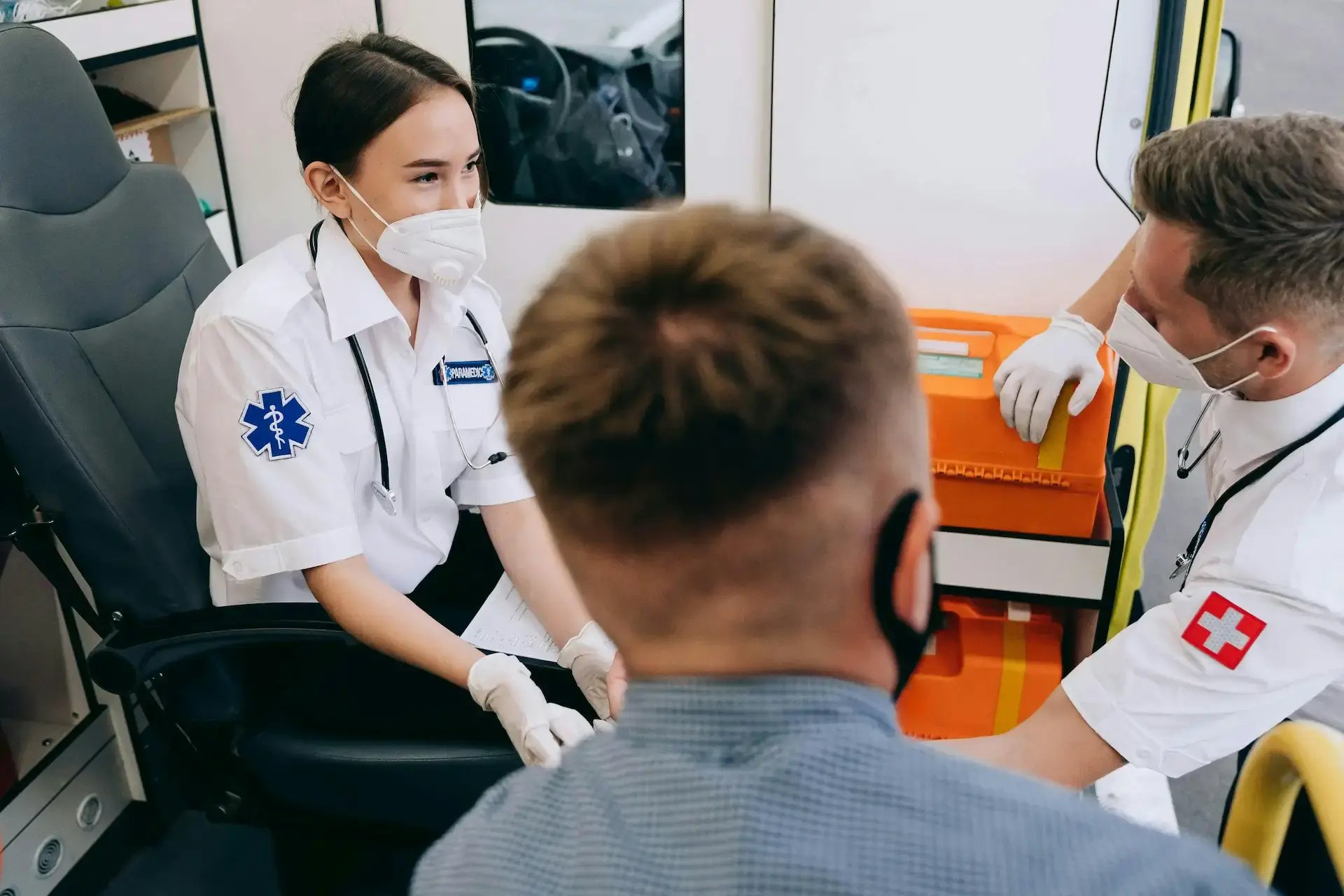 deux paramédicaux et un patient masqués discutent dans l'ambulance