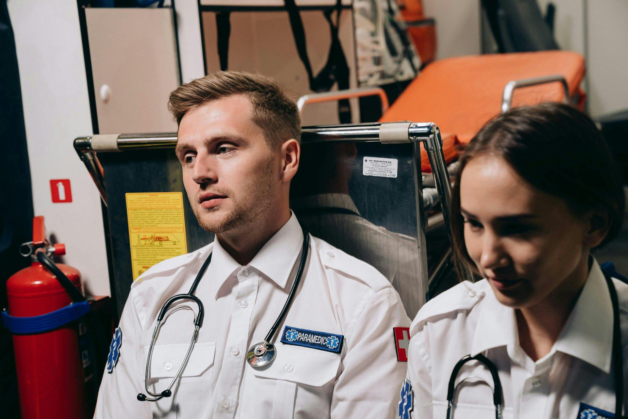 Deux paramédicaux en uniforme à l'intérieur d'une ambulance, avec brancard et extincteur visibles