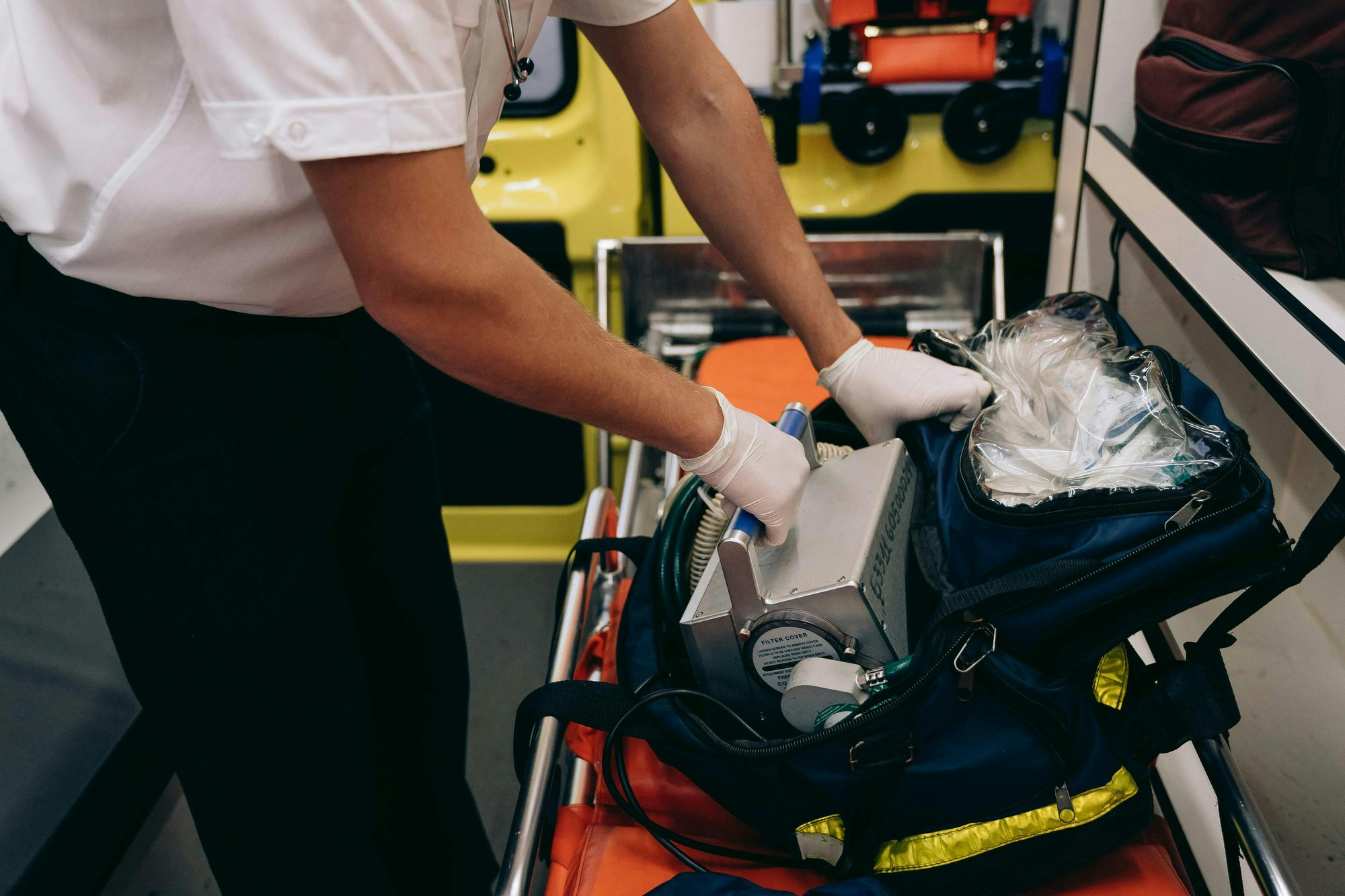 Un paramédical ganté prépare du matériel médical sur un brancard dans une ambulance.