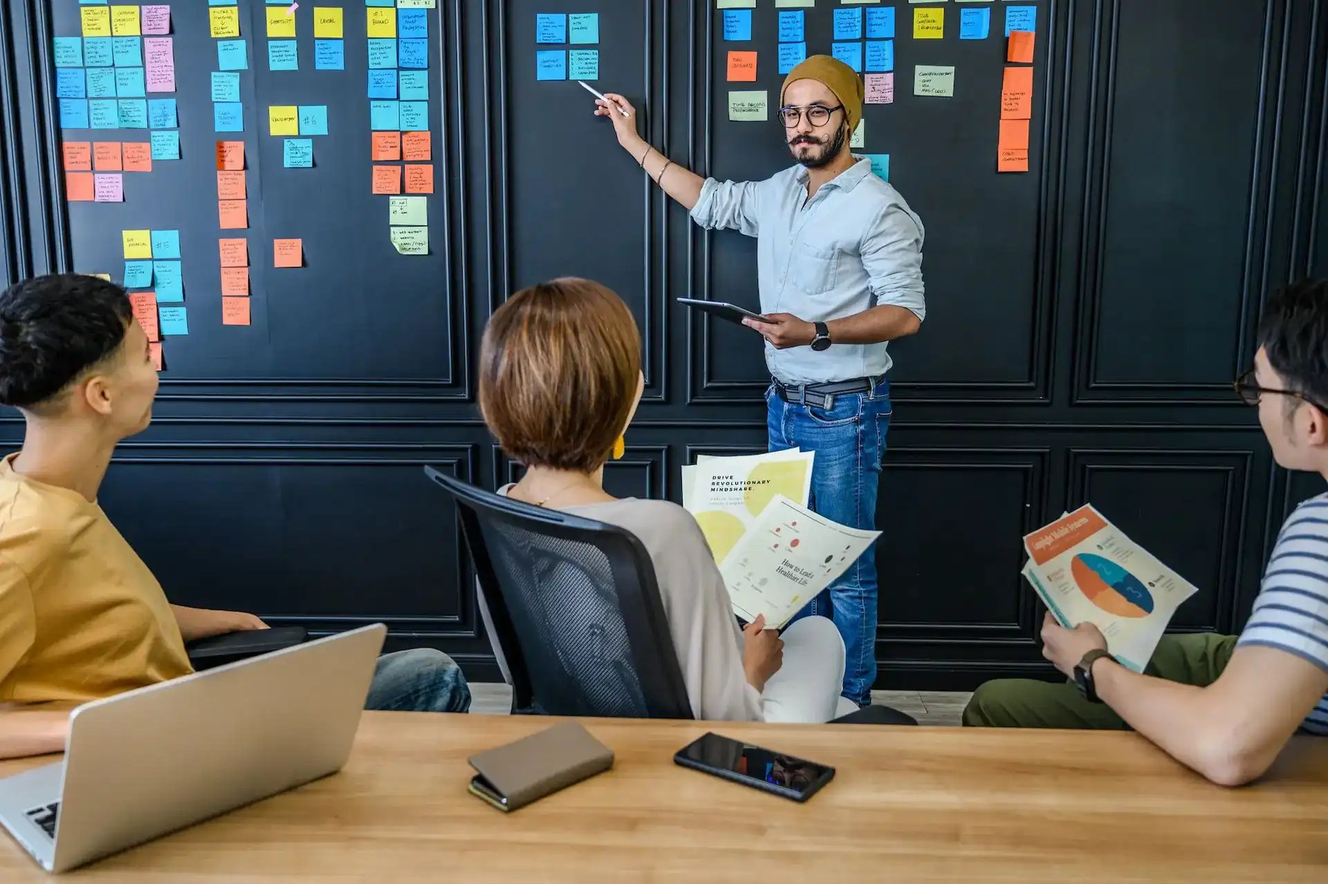 Un chef de projet présente un plan à son équipe avec des post-it au mur